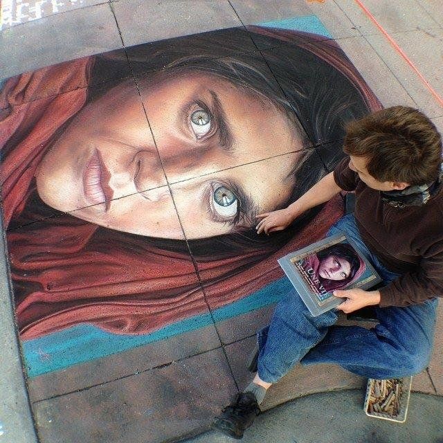 A large chalk portrait drawn on the pavement, with the artist working at its edge.